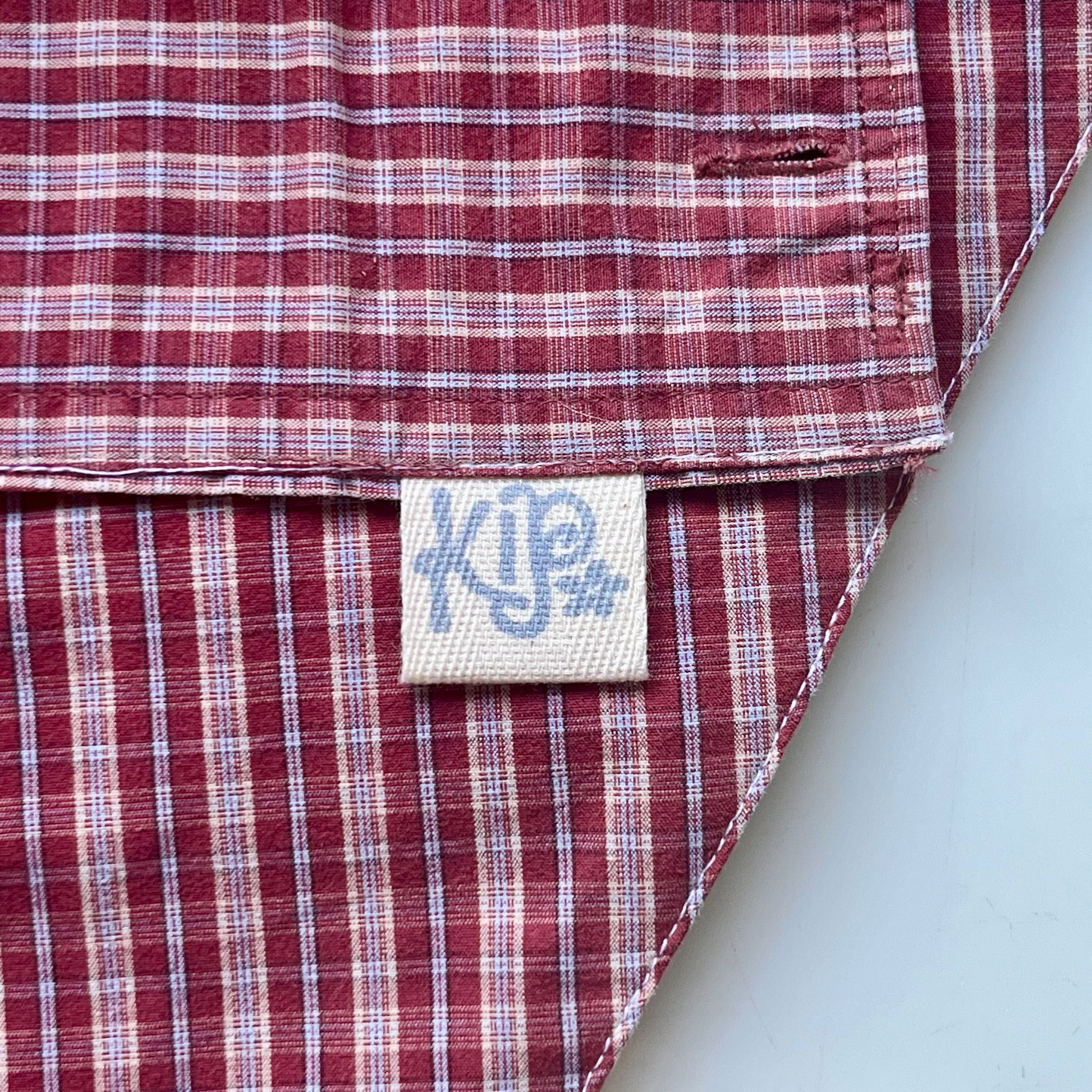 Close-up of a red and white checkered shirt with a visible brand label on a marble background