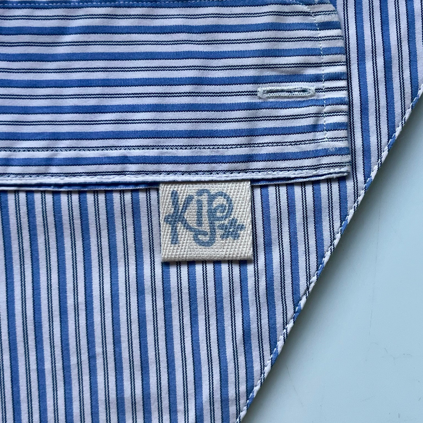 Close-up of a blue and white striped shirt with a brand label on a marble background